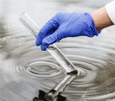 Researcher holds a test tube with water in a hand in blue glove